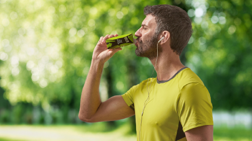 Hombre deportista bebiendo de un envase de cartón para bebidas sobre fondo verde